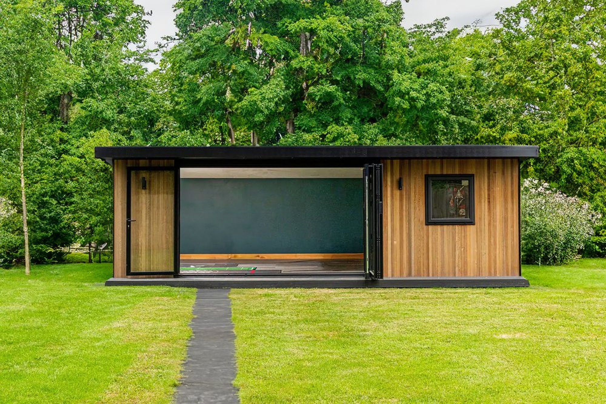 Vertical wood Cladded Garden Room with anthracite bifold doors surrounded by luscious green garden